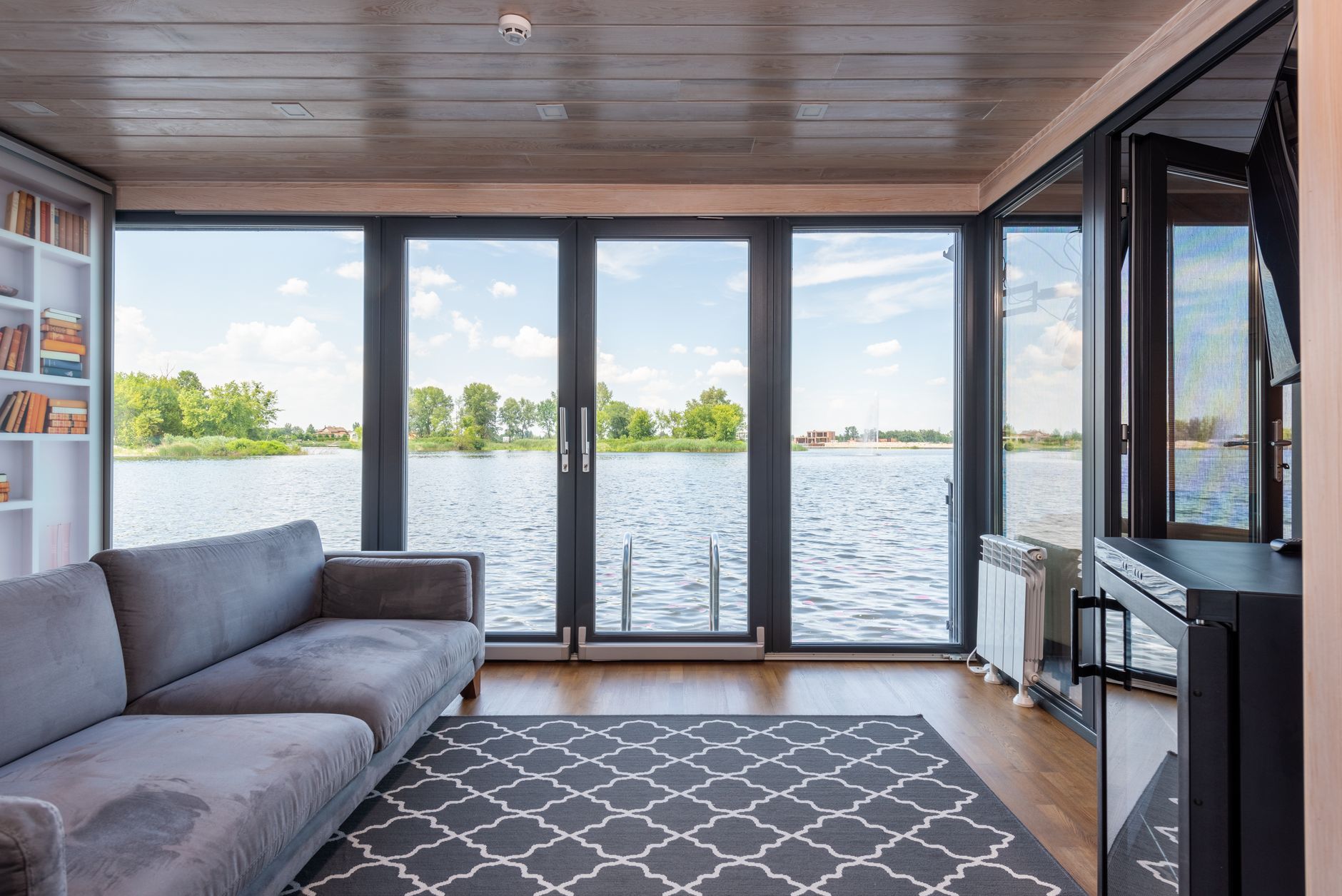Salón con grandes ventanales de marco oscuro de suelo a techo con vistas a un lago sereno