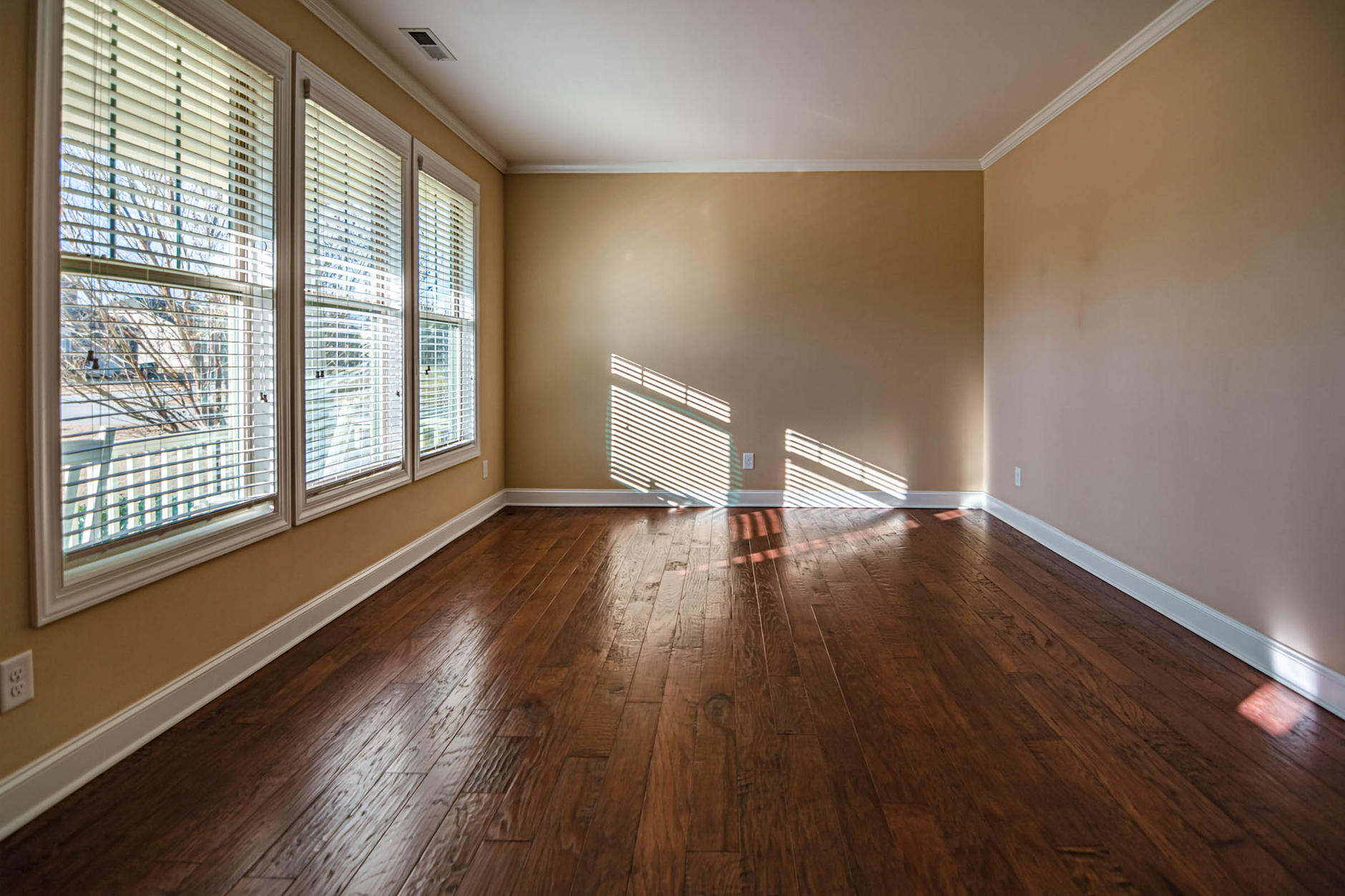 Sala vacía con suelo de madera donde la luz del sol entra por una hilera de ventanas y dibuja franjas cálidas sobre el parquet