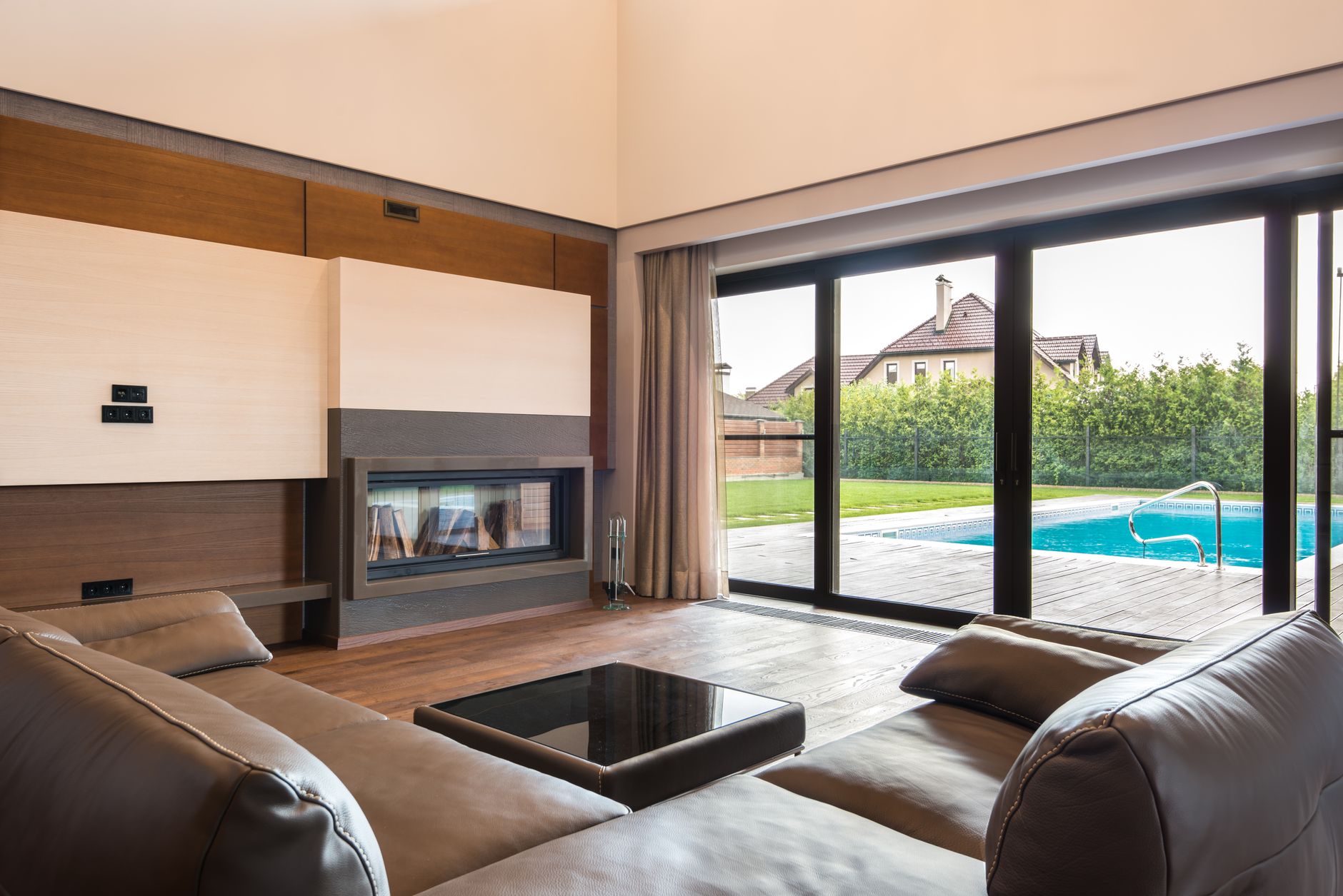Salón con grandes puertas correderas de marco oscuro abiertas hacia una terraza con piscina y jardín